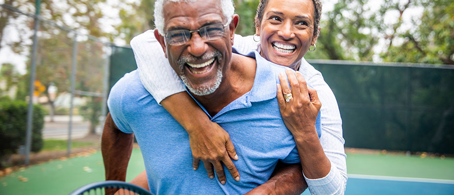 Elderly couple hugging and laughing on a tennis court