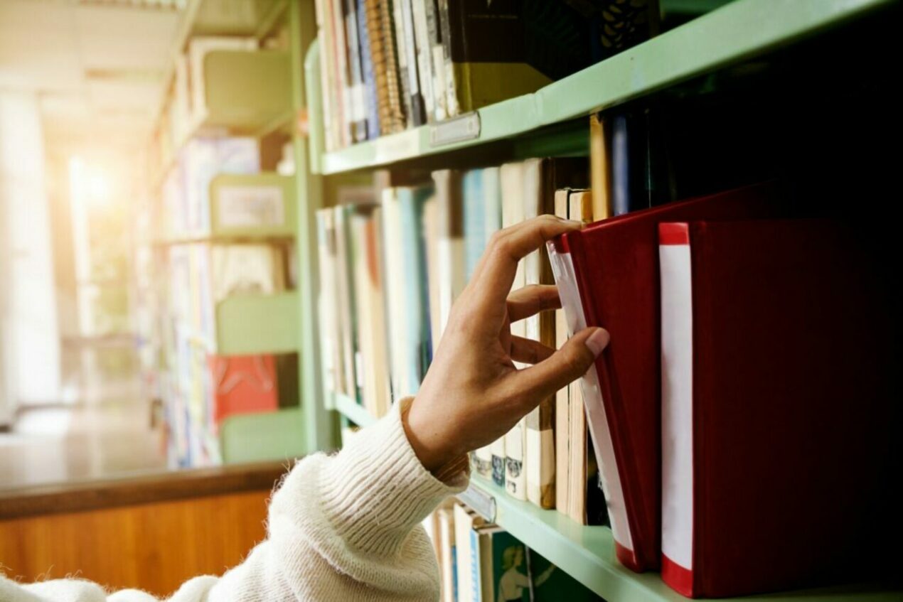 a hand choosing a book of a shelf at a library