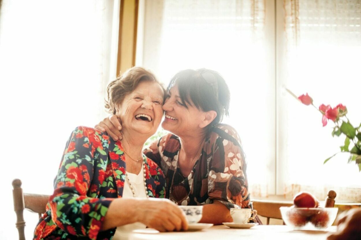 A senior woman and her adult daughter laugh together.